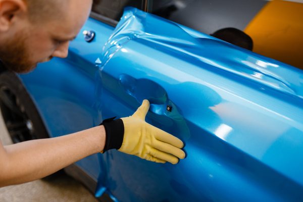 Protective vinyl foil or film installation process, car wrapping. Worker makes auto detailing. Automobile paint protection, professional tuning