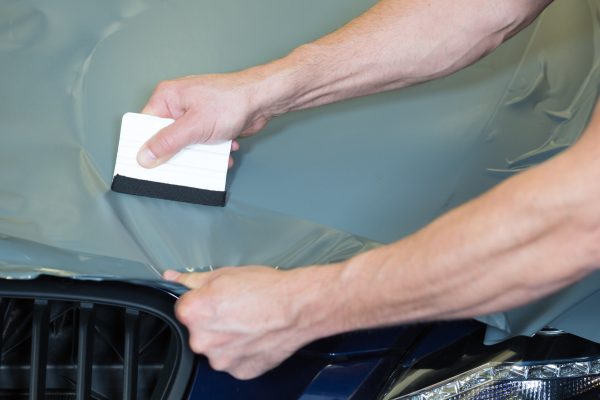 Car wrappers using squeegee to straighten vinyl foil